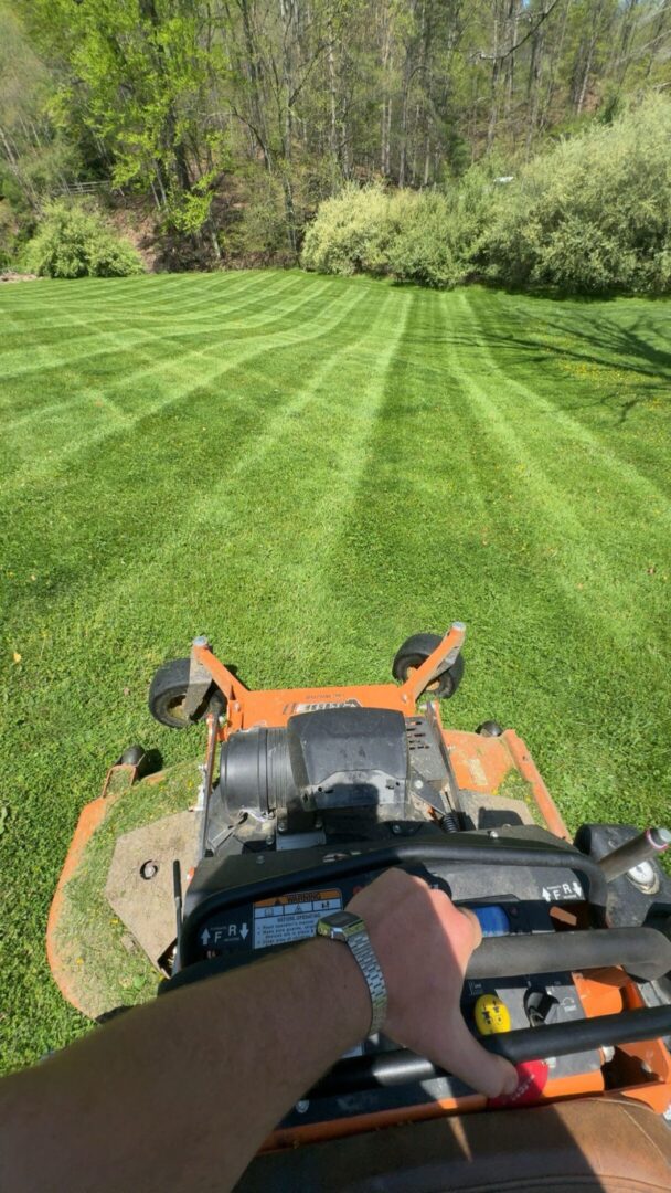 Riding lawn mower cutting green grass stripes.